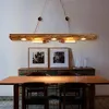 A dining room with a wooden table and chairs, a sideboard with artwork, and a rustic wooden chandelier. Produktbild-Vorschau
