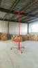 A red drywall lift is standing in a warehouse with boxes stacked in the background. Anteprima dell’immagine prodotto