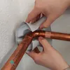Hands are shown applying a protective insulation material around copper pipes and a 90-degree elbow joint. Produktbild-Vorschau