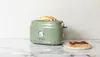 A green Haden toaster with toast in it sits on a marble countertop next to a slice of toast with jam. Náhled obrázku produktu