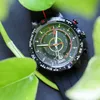 A close-up shot of a Timex watch with a compass dial, partially obscured by green leaves. Podgląd zdjęcia produktu