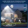 A modern house at night, illuminated by a large solar street lamp. A person walks on the driveway, and a dog plays with a frisbee. Produktbild-Vorschau