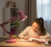 A young girl is doing homework at a desk under a pink desk lamp. Anteprima dell’immagine prodotto