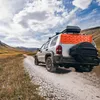 A silver SUV is driving on a dirt road in a mountainous landscape, with an orange traction board attached to the rear. Náhled obrázku produktu