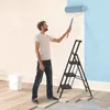 A man is painting a wall with a roller while standing on a step ladder. A white bucket is on the floor. Voir les images du produit