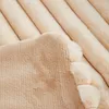 A close-up view of a soft, plush blanket with a ribbed texture on one side and a fluffy, faux fur texture on the other, showing a decorative edge with pom-poms. Produktbild-Vorschau