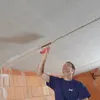 A man is applying plaster to a ceiling with a trowel. Produktbild-Vorschau