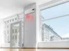 A modern living room with large windows, showcasing a wall-mounted air conditioner emitting red heat waves. Voir les images du produit