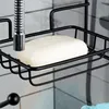 A close-up view of a black metal shower caddy holding a bar of soap, with a showerhead visible above it. Anteprima dell’immagine prodotto