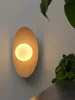 A wall lamp with a light bulb is mounted on a wall next to a plant. Podgląd zdjęcia produktu