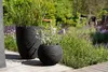 Two black planters with plants in a garden setting on a wooden deck. Náhľad obrázku produktu