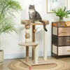 A cat is sitting on a cat tree next to a plant and a storage unit. Anteprima dell’immagine prodotto