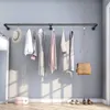 A wall-mounted clothing rack with several garments and a handbag hanging on it, set against a gray wall with sunlight casting shadows. Produktbild-Vorschau