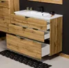 A modern bathroom vanity with a white sink and wooden drawers against a dark wall, with a black rug on the floor. Produktbild-Vorschau