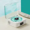 A vintage-style portable speaker with a clear blue lid and turntable, placed on a sandy surface next to a body of water. Podgląd zdjęcia produktu