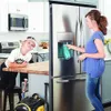A woman is filling a water bottle from a refrigerator dispenser, while a young boy in a baseball cap watches. Produktbild-Vorschau