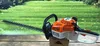 A Stihl hedge trimmer is placed on a wooden surface with a green grassy background. Produktbild-Vorschau