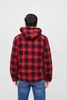 A person seen from behind wearing a red and black checkered hooded jacket and blue jeans against a white background. Náhled obrázku produktu