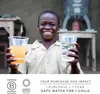 A young boy smiles while holding two cups, one with orange liquid and the other with clear liquid, in front of a water filtration system. Produktbild-Vorschau