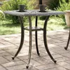 A square outdoor table with two cups on it, set on a patio with greenery in the background. Produktbild-Vorschau