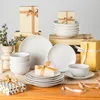 A collection of white ceramic dinnerware with a hexagonal pattern, arranged with gift boxes and ribbons on a wooden surface. Náhled obrázku produktu