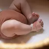 A close-up shot of a baby's legs and feet, with one foot wearing a pink Owlet Dream Sock device. Produktbild-Vorschau