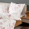 A close-up view of a bed with floral patterned bedding and a bedside table with a vase. Produktbild-Vorschau