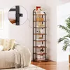 A tall, narrow bookshelf with dark metal framing and wood shelves is placed next to a cream-colored sofa and a large green plant. The top shelf has a framed picture and a vase of flowers. Produktbild-Vorschau