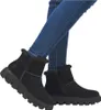 A pair of black winter boots worn by a person wearing blue jeans. Voir les images du produit