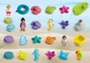 A collection of small toys and figures, many with a sea or beach theme, arranged on a sandy background with a blue water background. Náhľad obrázku produktu