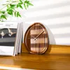 A wooden clock with an organic shape sits on a wooden shelf next to a stack of magazines, with a plant in the upper left corner. Voir les images du produit