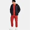 A man wearing a black puffer jacket and red sweatpants. Produktbild-Vorschau