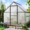 A greenhouse in a garden setting with plants and gardening tools. Voir les images du produit