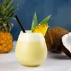 A cocktail with pineapple and coconut garnishes, with a pineapple and coconut in the background. Produktbild-Vorschau
