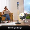 A woman is sitting on a couch using a laptop, with a vacuum cleaner standing nearby. A cat is lying on the floor. Produktbild-Vorschau
