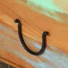 A close-up view of a black metal handle attached to a wooden surface with distressed paint. Produktbild-Vorschau