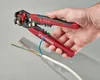 A hand holding a wire stripper tool over a cable with multiple wires. Produktbild-Vorschau