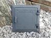 A cast iron access door for a chimney or oven, placed on a bed of gravel with rocks in the background. Produktbild-Vorschau