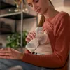 A woman is sitting and using a Philips AVENT hand breast pump. Produktbild-Vorschau