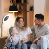 A family is sitting on a couch in a living room, with a fan and light in the foreground. Anteprima dell’immagine prodotto