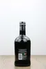 A dark glass bottle of The Pogues Irish Whiskey is shown from the back against a white background, resting on a wooden surface. Produktbild-Vorschau