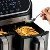 A hand is pouring oil onto french fries in an air fryer. Podgląd zdjęcia produktu