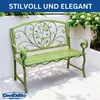 A green metal garden bench with ornate scrollwork and leaf motifs, set against a white wall with greenery and flowers. Podgląd zdjęcia produktu