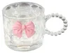 A clear glass mug with a pink bow decoration and a beaded handle, isolated on a white background. Anteprima dell’immagine prodotto