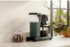 A green MOCAMASTER coffee maker is shown on a kitchen counter next to a jar of coffee beans and a plant. Náhled obrázku produktu