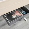 A close-up view of an open desk drawer containing a book, a ruler, and blue scissors. Produktbild-Vorschau