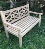 A wooden bench is placed outdoors on a grassy area with trees and foliage in the background. Produktbild-Vorschau
