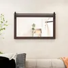 A rectangular mirror with a dark brown wooden frame and a black sliding barn door hardware is mounted on a light-colored wall above a sofa with decorative pillows. A green plant is visible to the left of the mirror, and a white shelf with boxes is reflecte Podgląd zdjęcia produktu