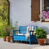 A blue wooden garden bench with a blanket and book on it, placed on a patio next to potted plants and a house. Anteprima dell’immagine prodotto