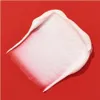A swatch of white cream with pink undertones is smeared on a red background. Podgląd zdjęcia produktu
